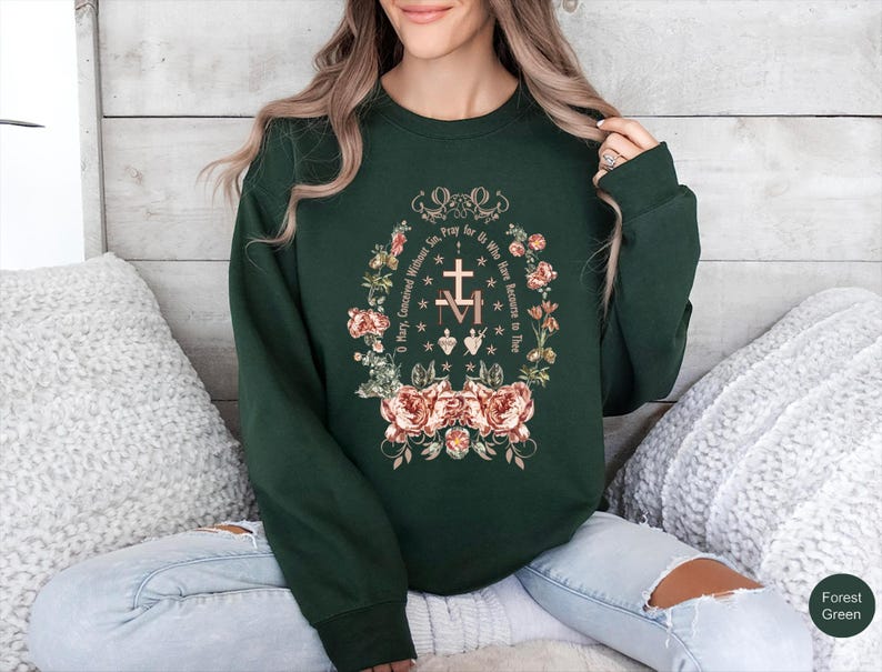 May include: Forest green sweatshirt with a floral design. The design includes a cross, hearts, and the text "O Mary, Conceived Without Sin, Pray for Us Who Have Recourse to Thee."