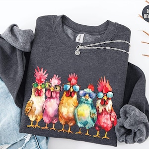May include: Dark heather grey sweatshirt with a graphic of five colorful chickens wearing sunglasses. The chickens are arranged in a row and are facing forward. The sweatshirt has a crew neck and long sleeves.
