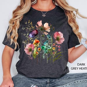May include: Dark grey heather t-shirt featuring a watercolor floral design. The design includes pink, orange, purple, and blue flowers with green stems and leaves. The text "DARK GREY HEATHER" is printed on the bottom right.