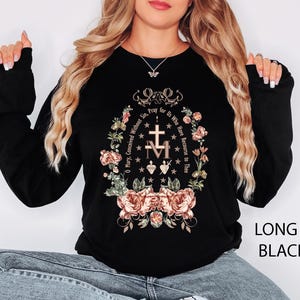 May include: Black long-sleeve shirt with a floral and religious design. The design includes a cross, the letters "M" and "T", and the text "O Mary, Conceived Without Sin, Pray for Us Who Have Recourse to Thee."