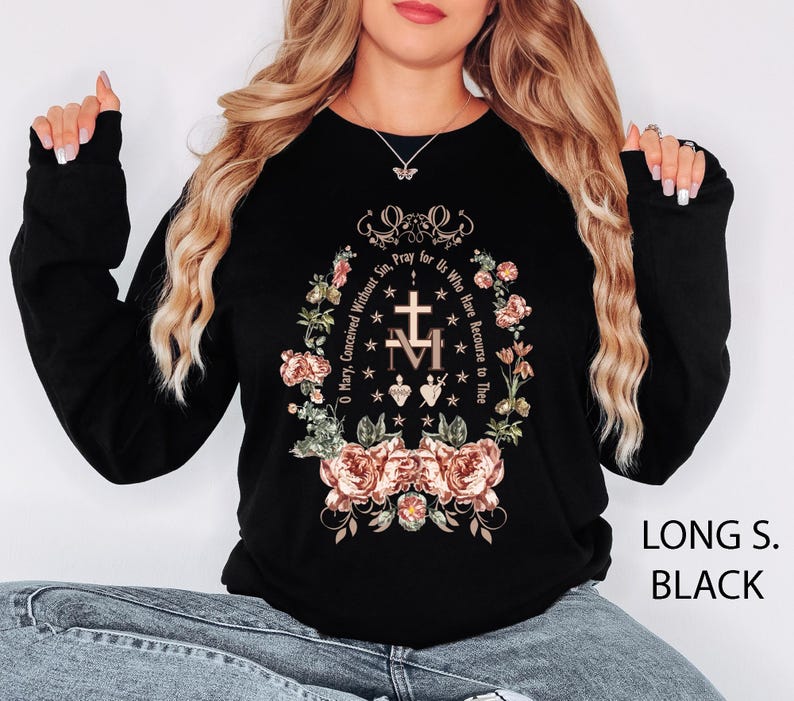 May include: Black long-sleeve shirt with a floral and religious design. The design includes a cross, the letters "M" and "T", and the text "O Mary, Conceived Without Sin, Pray for Us Who Have Recourse to Thee."