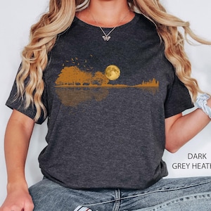 Pode incluir: T-shirt cinza escuro mesclada com um design de paisagem. Apresenta uma lua cheia, &aacute;rvores e p&aacute;ssaros em voo, em tons de ouro e marrom. O design reflete-se abaixo. O texto "DARK GREY HEATHER" &eacute; vis&iacute;vel.