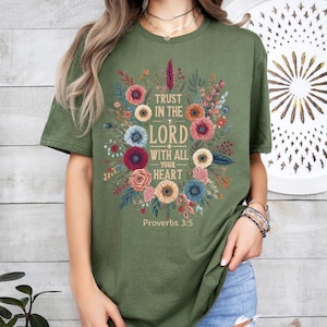 May include: Olive green t-shirt featuring a floral design with the text "Trust in the Lord with all your heart" and "Proverbs 3:5". The design includes colorful flowers and foliage.
