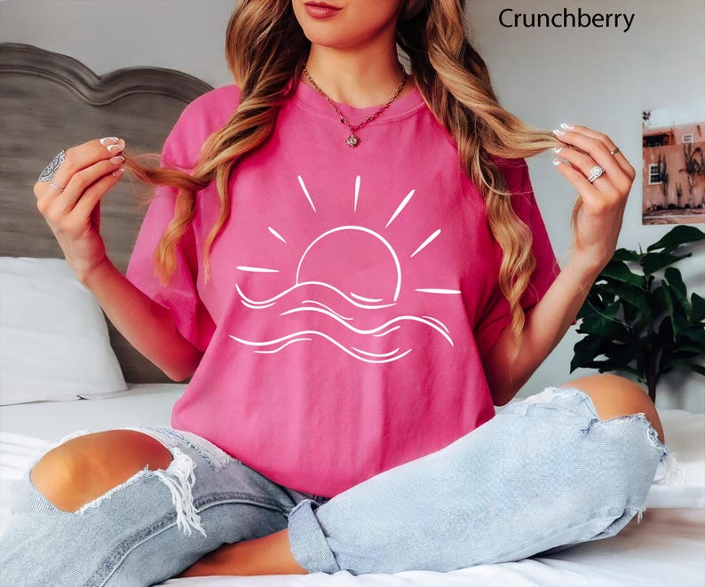 Pu&ograve; includere: Una t-shirt a maniche corte rosa acceso con una grafica a linee bianche che raffigura un sole che sorge sopra le onde dell'oceano. La maglietta ha un girocollo ed &egrave; abbinata a jeans in denim azzurro consumato con strappi sfilacciati.