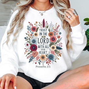 May include: White sweatshirt featuring a floral design with the text "Trust in the Lord with all your heart" and "Proverbs 3:5". The design includes colorful flowers and foliage in shades of red, blue, and yellow.