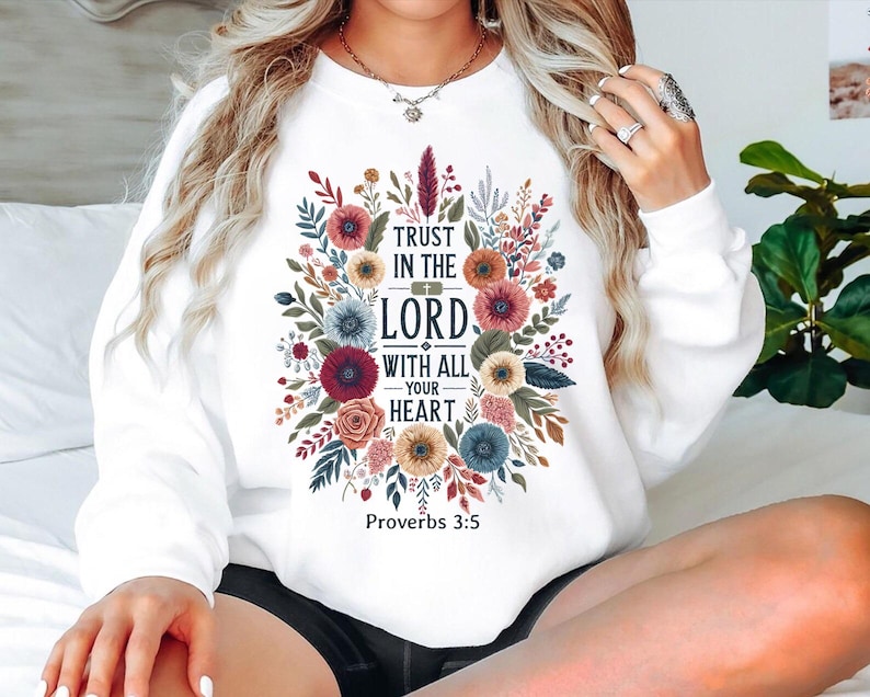 May include: White sweatshirt featuring a floral design with the text "Trust in the Lord with all your heart" and "Proverbs 3:5". The design includes colorful flowers and foliage in shades of red, blue, and yellow.