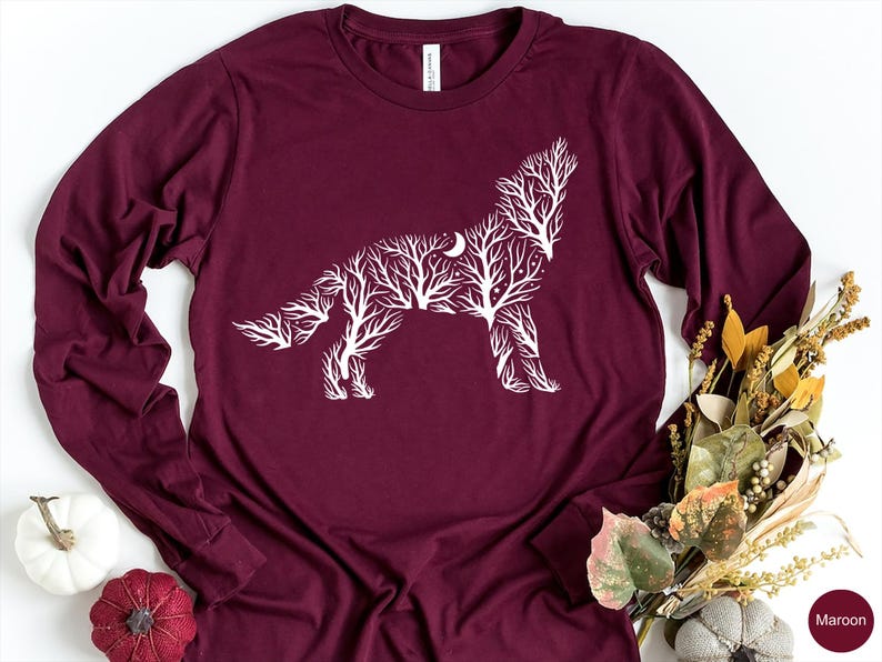 May include: Maroon long-sleeve shirt featuring a white wolf design. The wolf is created from a tree branch pattern with a crescent moon. The shirt is a comfortable, casual style.