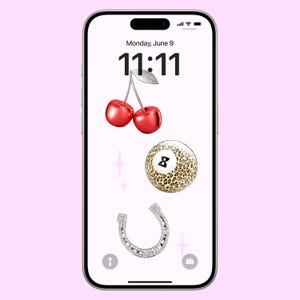 Könnte beinhalten: Ein Smartphone-Bildschirm zeigt die Uhrzeit 11:11 mit dem Datum Montag, 9. Juni. Der Bildschirm zeigt auch drei Emojis: ein Paar rote Kirschen, eine 8-Ball mit Leopardenmuster und ein silbernes Hufeisen mit Diamanten.