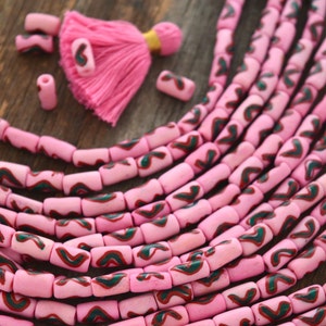 以下が含まれることがあります： ピンクとグリーンのガラスビーズで、渦巻き模様が施されています。ビーズはネックレスやブレスレットになるように糸に通されています。