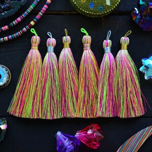 May include: Seven colorful tassels with pink, green, and yellow stripes. The tassels are made of soft, silky threads and have a metallic gold trim.