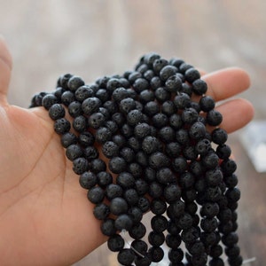 May include: A strand of black lava rock beads. The beads are round and have a rough, textured surface.