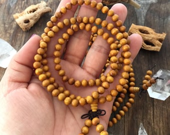 May include: A wooden prayer bead mala necklace with brown beads and a knotted tassel. The mala is made of natural wood and has a warm, earthy tone.