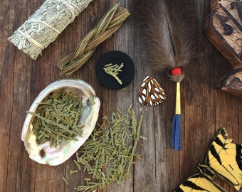 May include: A collection of smudging tools and herbs, including sage, cedar, and a feather. The tools are laid out on a wooden surface with a butterfly in the lower right corner.