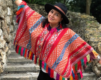 Könnte beinhalten: Eine Frau trägt einen bunten, gefranstem Poncho mit geometrischen Mustern. Sie steht auf Steinstufen und trägt einen schwarzen Hut.