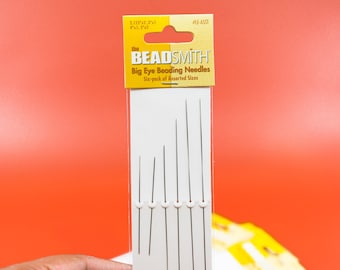 Op de afbeelding: Een verpakking met zes kralen naalden in verschillende maten met grote ogen. De verpakking is geel en wit met de tekst "the BEADSMITH Big Eye Beading Needles Six-pack of Assorted Sizes" en het productnummer "#LE-ASST".