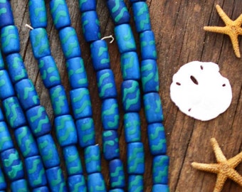 May include: A strand of blue and green wooden beads with a wavy pattern. The beads are arranged in a cascading pattern on a wooden surface.