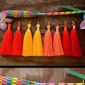 May include: Assortment of colorful silk tassels in red, orange, yellow, and pink. The tassels are arranged in rows on a wooden surface.