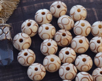 May include: A collection of white bone beads with brown circle designs. The beads are arranged on a dark brown wooden surface.