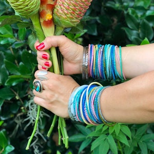 May include: A bouquet of pink and white roses and orange ginger flowers with green stems, held by a person wearing colorful bracelets.