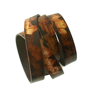 May include: A close-up of a brown leather bracelet with a camouflage pattern. The bracelet is made of multiple strands of leather that are woven together.