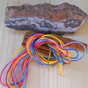 May include: A close-up of colorful cords wrapped around cinnamon sticks. The cords are blue, yellow, pink, and red. The cords are on a light brown wooden surface.