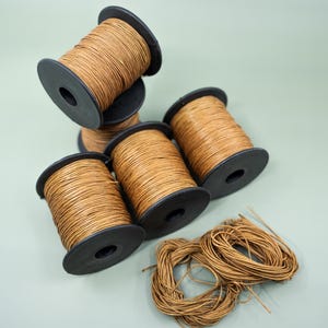 May include: Five spools of brown waxed cord, wound on black plastic spools, with a loose pile of the cord in the foreground.