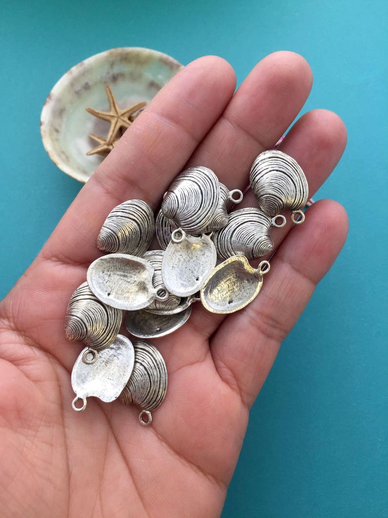 May include: A collection of silver-toned metal clam shell charms with a loop for attaching to jewelry or other crafts.
