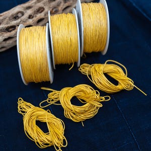 May include: Four spools of yellow waxed cord, with three stacked on top of each other and one lying flat on a dark blue surface. Three additional lengths of cord are lying loose on the surface.