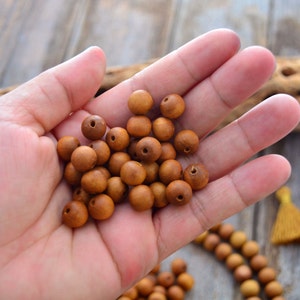 May include: A hand holding a pile of brown wooden beads. The beads are round and have a small hole in the center. The beads are arranged in a random pattern.