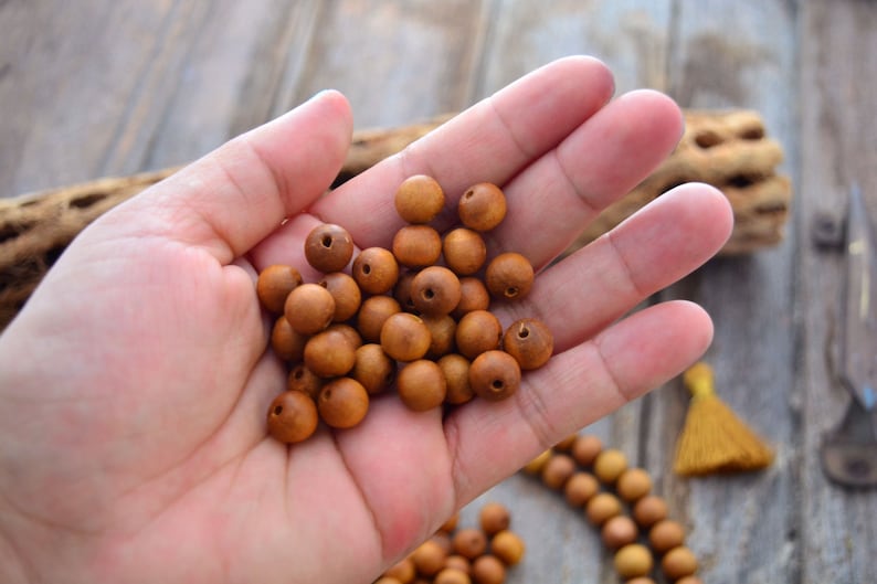 May include: A hand holding a pile of brown wooden beads. The beads are round and have a small hole in the center. The beads are arranged in a random pattern.