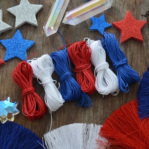 May include: Red, white, and blue craft supplies for making patriotic decorations.  The supplies include yarn, tassels, glitter stars, and iridescent crystals.