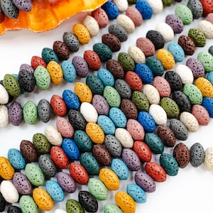 May include: A collection of colorful lava rock beads in various shades of blue, green, red, yellow, brown, and white. The beads are oval shaped and have a rough, porous texture.