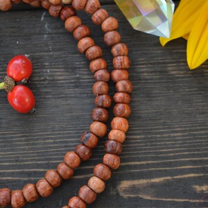 May include: A close-up of a wooden mala necklace with brown beads. The necklace is lying on a dark wooden surface.