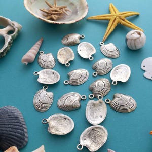 May include: A collection of silver-toned metal clam shell charms with a textured surface. The charms have a loop at the top for attaching to jewelry or other crafts.