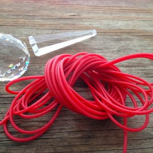 May include: A close-up of a red elastic cord, a clear crystal, and a clear prism on a wooden surface.