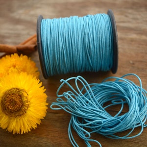 May include: A spool of light blue waxed cotton cord with a loose end of cord on a wooden surface.