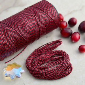 May include: A spool of red and black patterned cord with a small pile of red cranberries and a clear crystal star.