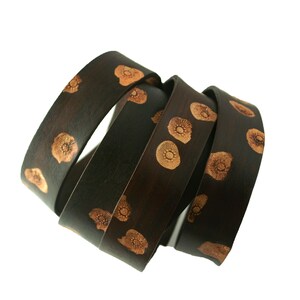May include: A set of four brown leather bracelets with a floral pattern in a light brown color.