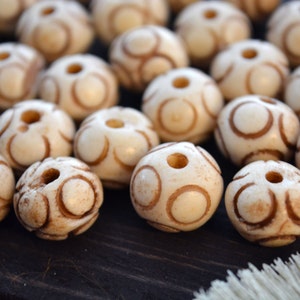 May include: A collection of white beads with brown circular patterns. The beads are smooth and have a hole in the center.