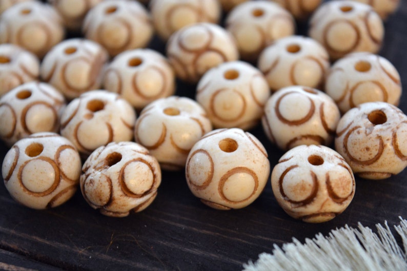 May include: A collection of white beads with brown circular patterns. The beads are smooth and have a hole in the center.