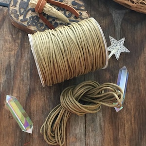 May include: A spool of olive green cord sits next to a tied bundle of the same cord. Two iridescent crystals and a star-shaped decoration are also present. A carved wooden piece and a leather-wrapped antler add to the rustic aesthetic.
