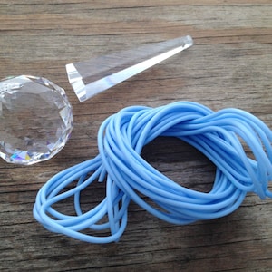 May include: A clear, faceted crystal ball, a clear, angled prism, and a coil of light blue rubber tubing are arranged on a wooden surface. The crystal ball reflects light, creating a rainbow effect. The tubing is tightly coiled.
