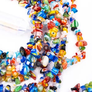 Op de afbeelding: Close-up van een ketting of armband gemaakt van kleurrijke glazen kralen. De kralen hebben verschillende vormen en maten, met een mix van rood, blauw, geel en groen. Op een witte achtergrond.