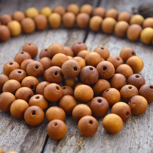 May include: A close-up of a pile of brown wooden beads. The beads are round and have a smooth, polished finish. They are arranged in a random pattern on a wooden surface.