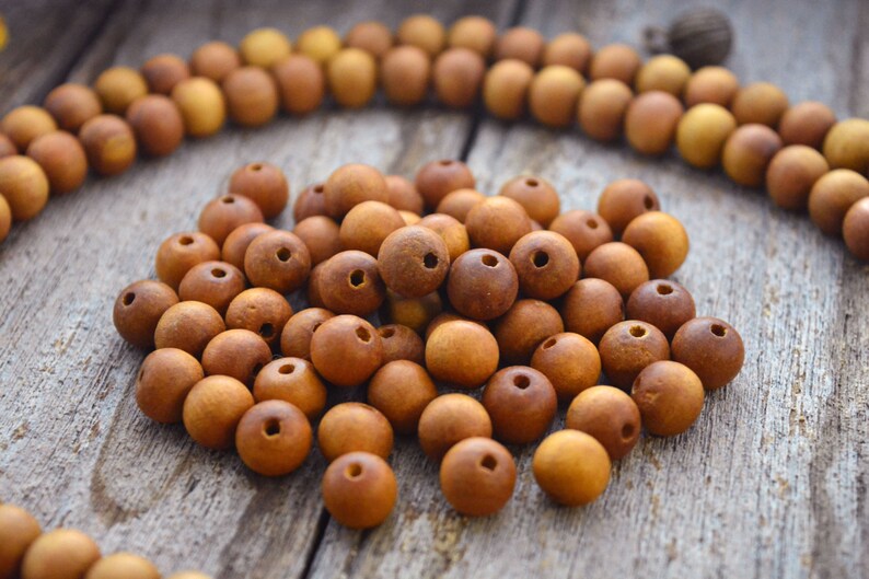 May include: A close-up of a pile of brown wooden beads. The beads are round and have a smooth, polished finish. They are arranged in a random pattern on a wooden surface.