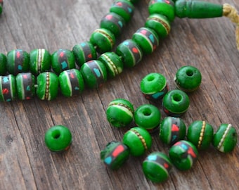 May include: A string of green beads with black, white, and red accents. The beads are strung on a cord and have a tassel at the end. There are also several loose beads on a wooden surface.
