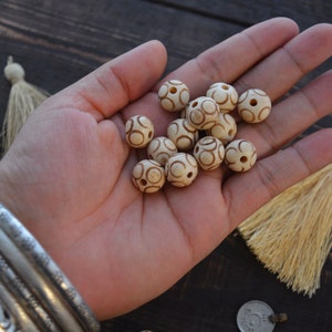 May include: A hand holding a collection of white wooden beads with brown circular patterns. The beads are approximately 1 inch in diameter.