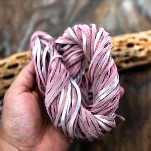 Puede incluir: Primer plano de un manojo de cordón de cuero rosa y blanco. El cordón es suave y flexible, y es perfecto para hacer joyas, pulseras u otros artículos de cuero.