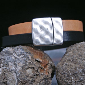 Puede incluir: Un brazalete de cuero de dos tonos con un cierre plateado texturizado. El brazalete est&aacute; hecho de cuero negro y marr&oacute;n.