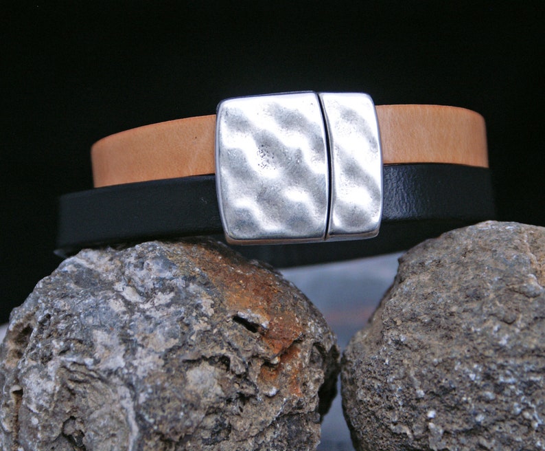 Puede incluir: Un brazalete de cuero de dos tonos con un cierre plateado texturizado. El brazalete est&aacute; hecho de cuero negro y marr&oacute;n.